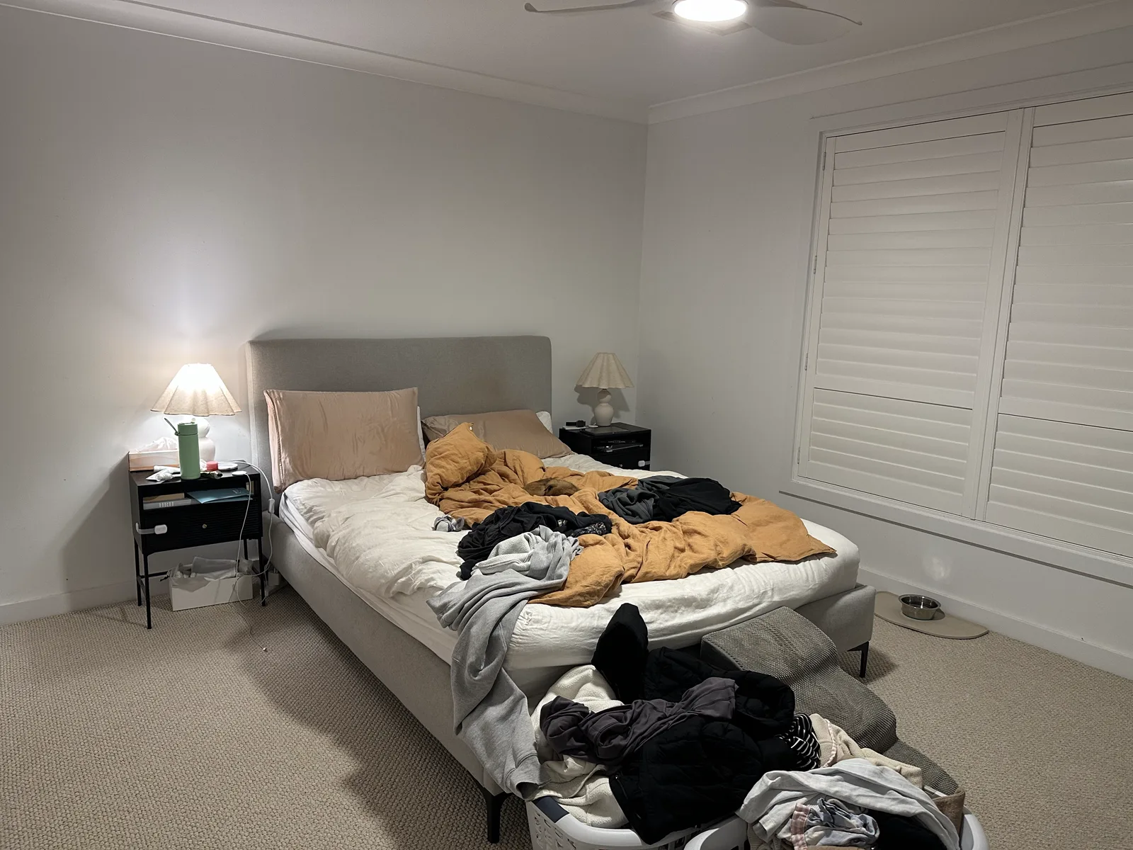 Main bedroom with an unmade bed, plantation shutters and beige carpet, before