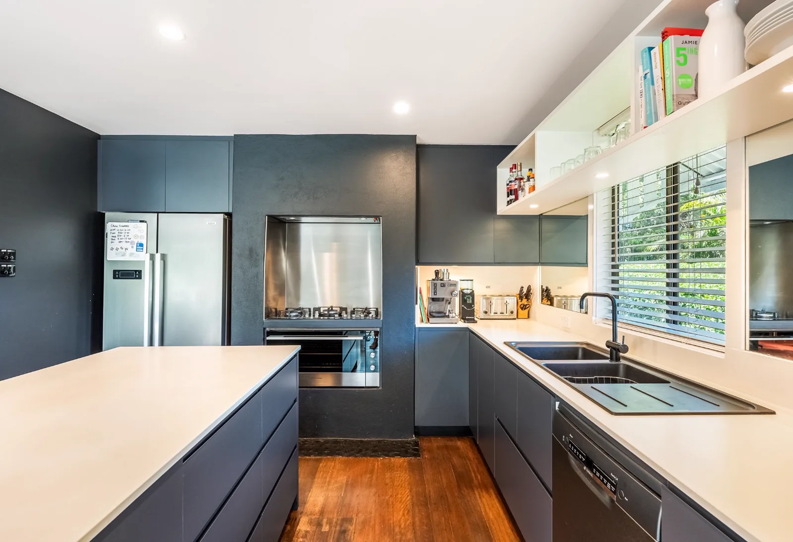 Galley kitchen with navy cabinetry, a pale benchtop and polished timber floorboards, before